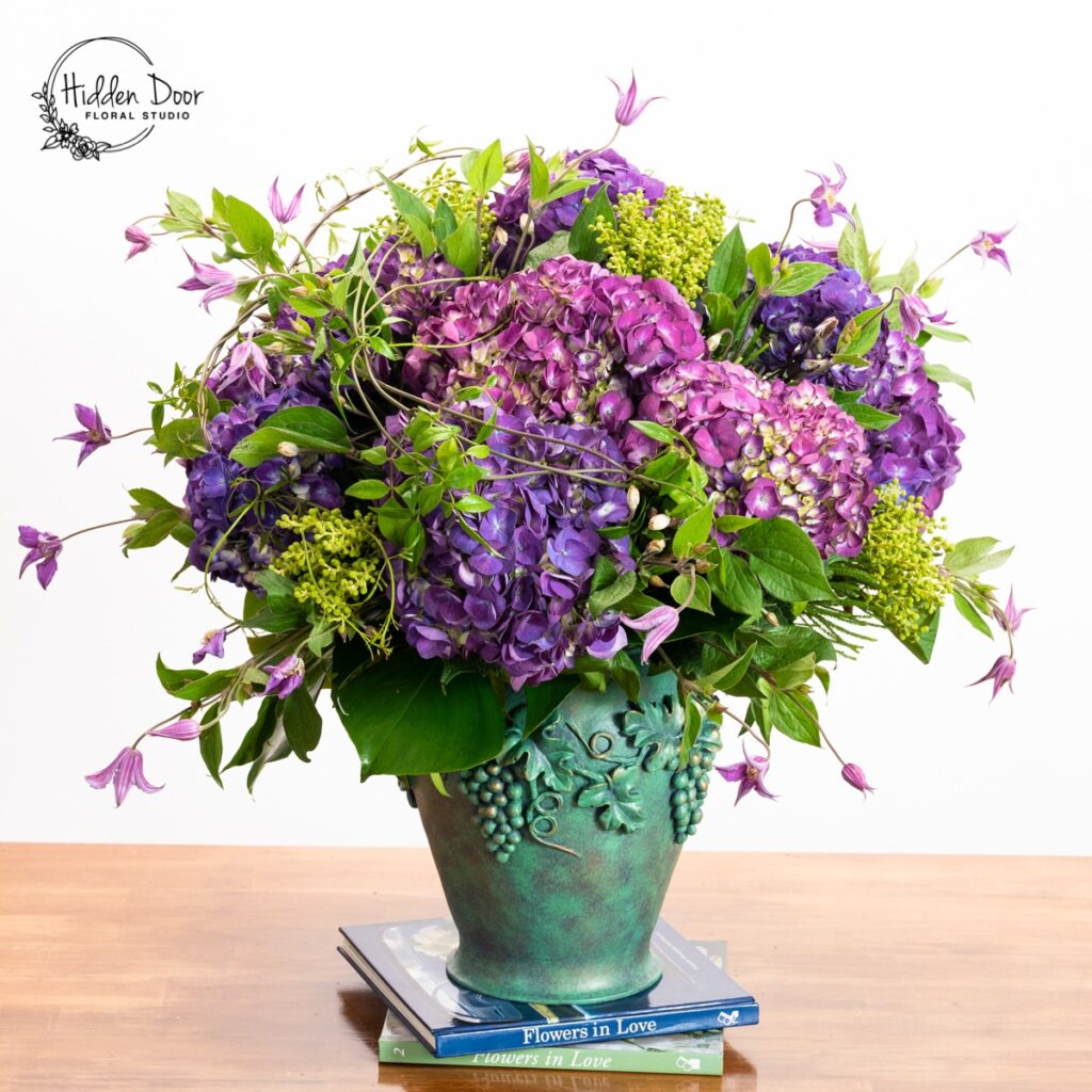 Purple hydrangea and green foliage floral arrangement in a decorative green vase
